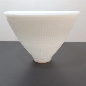 May include: A white, cone-shaped bowl with a textured, dotted pattern. The bowl has a wide opening and tapers down to a small, rounded base. The base has a slight orange hue.