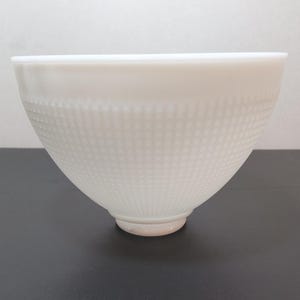 May include: A white, textured bowl with a dotted pattern. The bowl has a wide opening and tapers down to a small, rounded base. The bowl is made of a solid, opaque material.