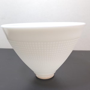 May include: A white ceramic bowl with a textured, dotted pattern on the lower half. The bowl has a wide, smooth rim and a conical shape, tapering to a small, rounded base. The bowl is likely for serving or display.