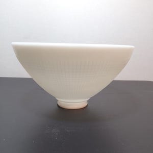 May include: A white, cone-shaped bowl with a textured grid pattern. The bowl has a rounded base with a slight pink hue. The bowl is sitting on a dark surface.