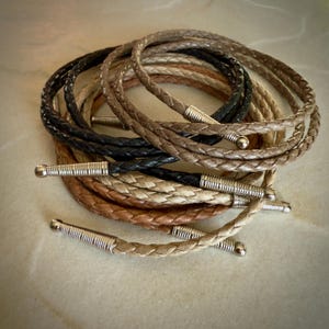 May include: A collection of braided leather cords with silver metal tips. The cords are in various shades of brown, beige, and black.