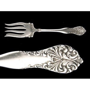 May include: A silver fork and knife with ornate, floral designs. The handles are intricately carved with swirling patterns.