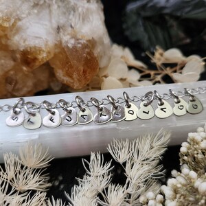 May include: A silver chain necklace with silver heart charms, each charm has a letter stamped on it, spelling out the word "STUART".