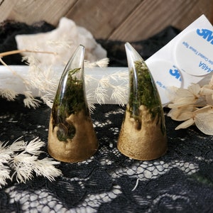 May include: Two resin horns with a gold base and green moss inside. The horns are on a black lace surface.