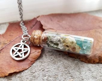 Könnte beinhalten: Eine silberne Halskette mit einem Pentagramm-Anhänger und einem kleinen Glasfläschchen, gefüllt mit klaren und grünen Kristallen und getrockneten Blumen.