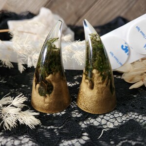 May include: Two clear resin horns with gold accents and green moss inside. The horns are sitting on a black lace surface.