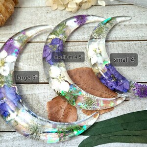 May include: Three crescent moon-shaped resin ornaments with pressed flowers. The largest is 5 inches, the medium is 4.5 inches, and the smallest is 4 inches.