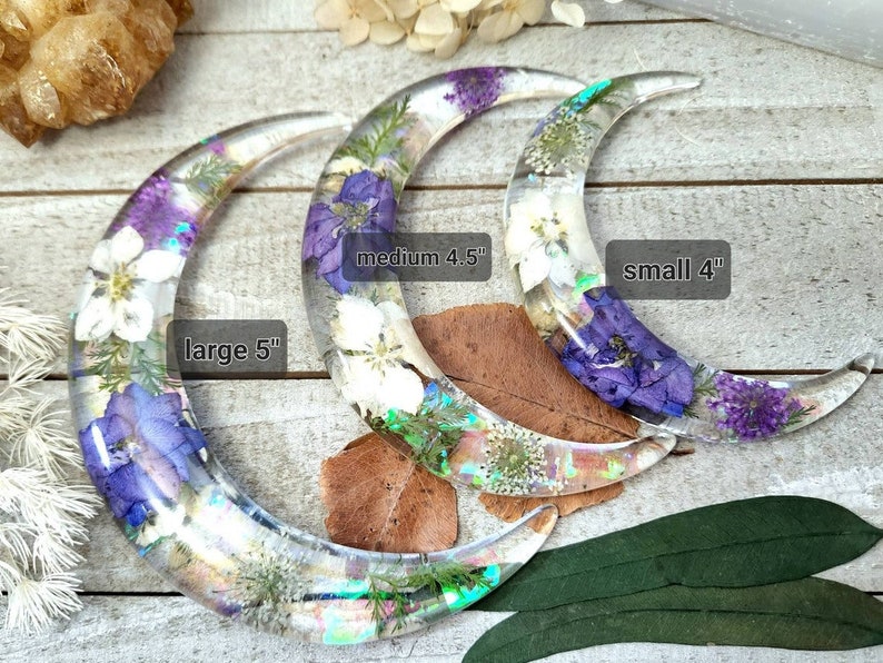 May include: Three crescent moon-shaped resin ornaments with pressed flowers. The largest is 5 inches, the medium is 4.5 inches, and the smallest is 4 inches.