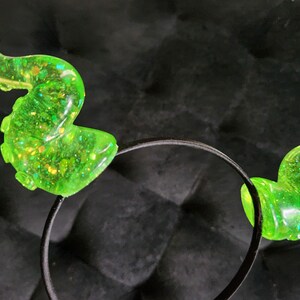 May include: A black headband with two green glitter octopus ears. The ears are translucent and have a sparkly finish.