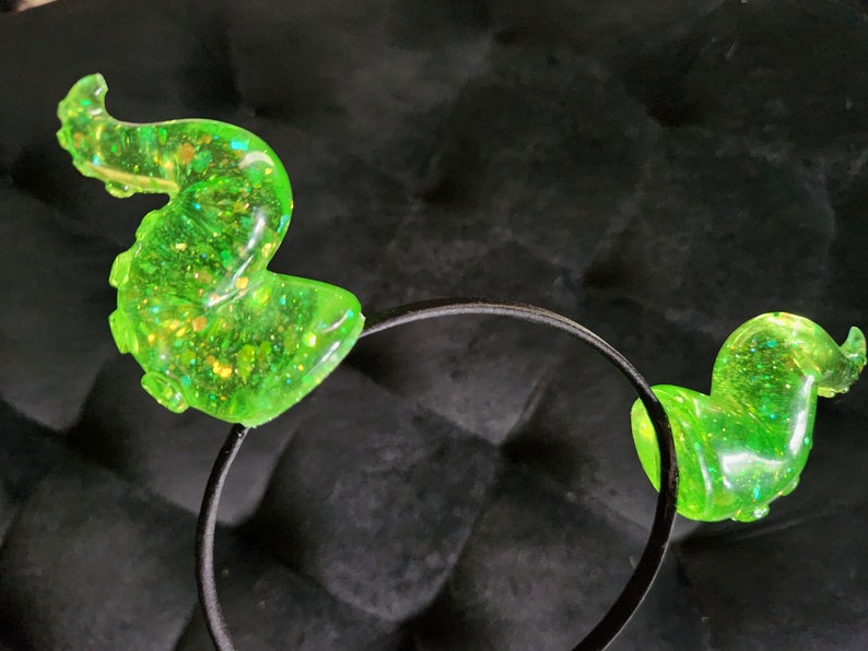 May include: A black headband with two green glitter octopus ears. The ears are translucent and have a sparkly finish.