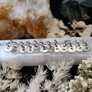 May include: A silver chain necklace with heart-shaped charms, each charm has a letter stamped on it, spelling out the word "FAITH".