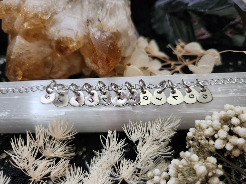 May include: A silver chain necklace with heart-shaped charms, each charm has a letter stamped on it, spelling out the word "FAITH".