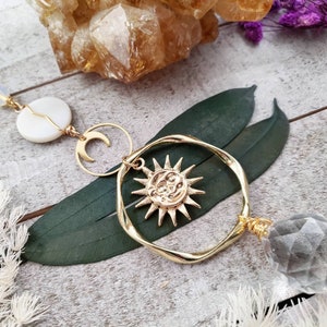 May include: Gold sun and moon charm necklace with a clear crystal pendant. The necklace features a delicate gold chain with a white shell charm and a crescent moon charm.