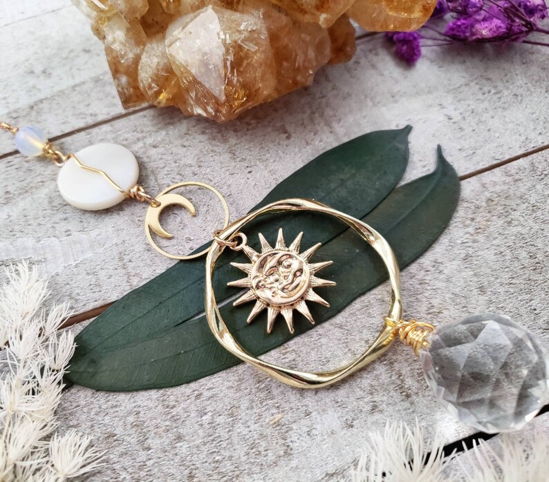 May include: Gold sun and moon charm necklace with a clear crystal pendant. The necklace features a delicate gold chain with a white shell charm and a crescent moon charm.