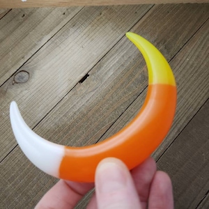 May include: A crescent-shaped, candy-colored, plastic ornament with a white, orange, and yellow color scheme.