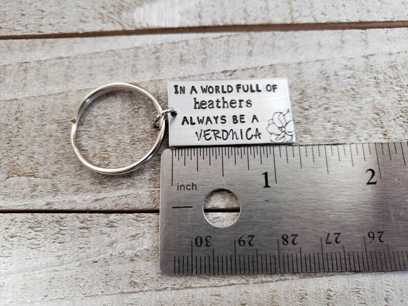 Pu&ograve; includere: Portachiavi d'argento con un'etichetta in metallo che recita "In un mondo pieno di eriche, sii sempre una Veronica". L'etichetta ha un piccolo disegno di fiore. Il portachiavi &egrave; accanto a un righello che misura 2,5 cm.
