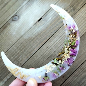 May include: A white crescent moon resin ornament with dried flowers and gold leaf accents.
