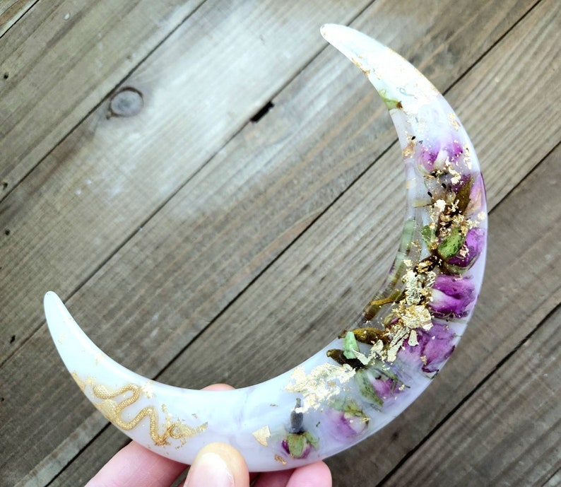 May include: A white crescent moon resin ornament with dried flowers and gold leaf accents.