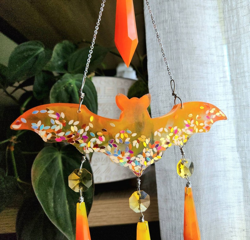 May include: Orange and glitter bat shaped resin suncatcher with crystal drops hanging from it.