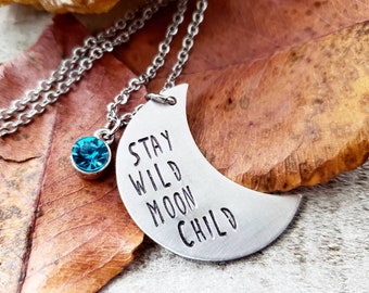 May include: A silver necklace with a crescent moon charm that says "Stay Wild Moon Child". The necklace also has a small blue crystal charm.
