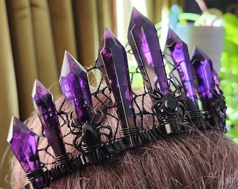 May include: A black crown with a spiderweb design and purple crystal points. The crown is made of wire and has a black velvet band.