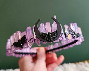 May include: A purple crystal crown with black moth and crescent moon accents. The crown is made of wire and crystals and is designed to be worn on the head.