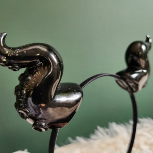 May include: Black headband with two octopus-shaped hair clips. The octopus is made of black resin with a glittery finish.
