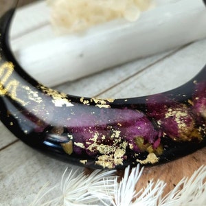 May include: A black crescent moon-shaped resin ornament with embedded dried flowers and gold leaf accents.