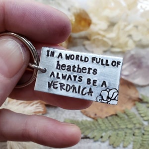 Pu&ograve; includere: Un portachiavi d'argento con il testo "In a world full of heathers always be a Veronica" e un piccolo disegno di fiore.