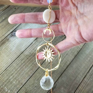 May include: Gold necklace featuring a sun and moon charm, a clear crystal pendant, and a white shell bead.