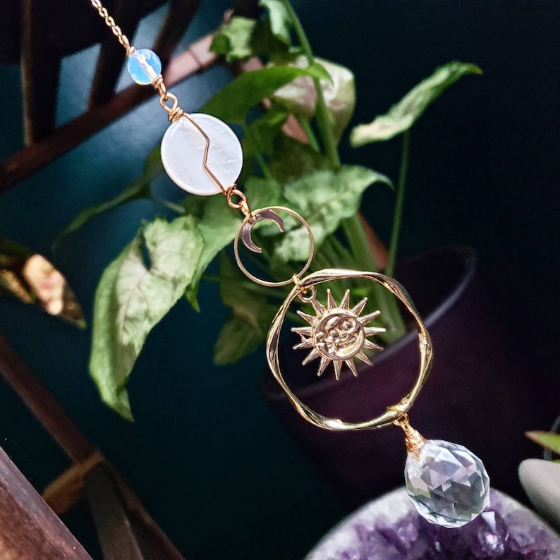 May include: Gold sun and moon charm with a white shell and clear crystal pendant. The charm hangs from a gold chain.