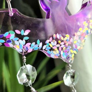 May include: A purple resin bat wind chime with iridescent glitter and crystal prisms hanging from it.