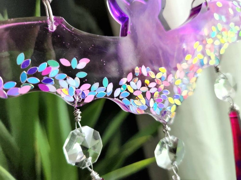 May include: A purple resin bat wind chime with iridescent glitter and crystal prisms hanging from it.