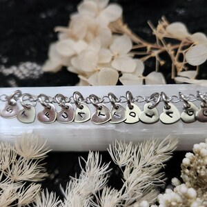 May include: A silver chain necklace with heart-shaped charms, each charm has a letter stamped on it, spelling out the word "TRUST".