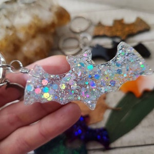 Pode incluir: Um chaveiro de morcego transparente com glitter iridescente e um anel de metal prateado. O morcego &eacute; feito de resina e tem um acabamento brilhante.