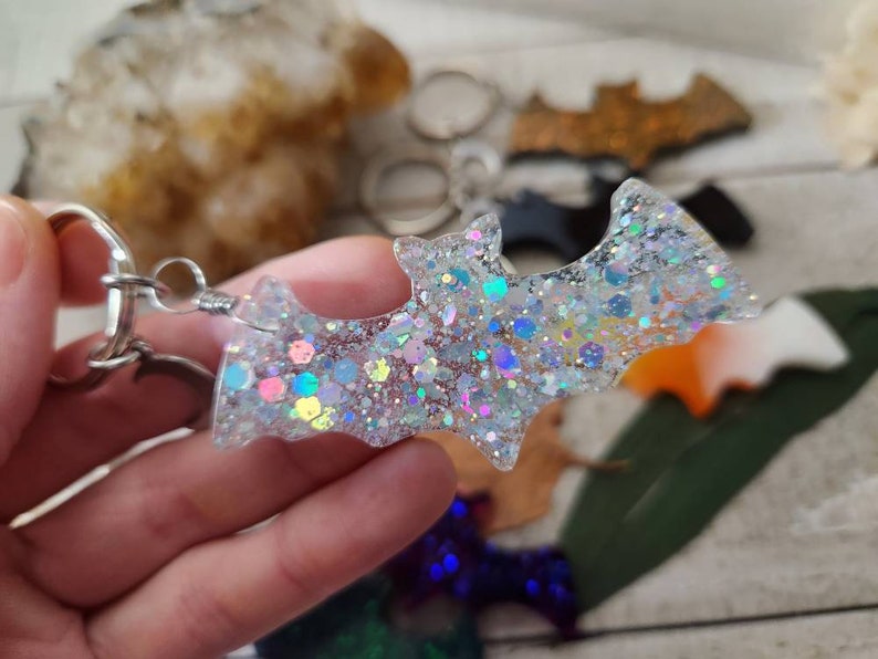 Pode incluir: Um chaveiro de morcego transparente com glitter iridescente e um anel de metal prateado. O morcego &eacute; feito de resina e tem um acabamento brilhante.