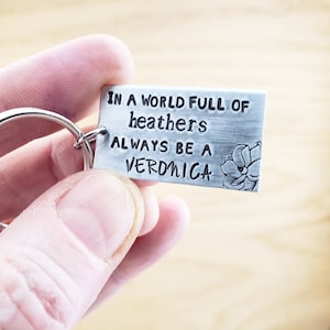 Pu&ograve; includere: Un portachiavi d'argento con un design a fiore e il testo "In un mondo pieno di erica, sii sempre una Veronica".