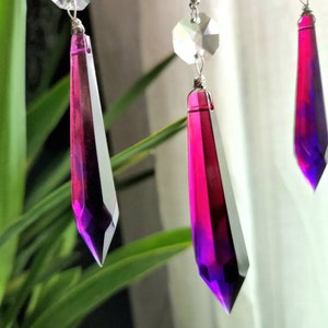 May include: Three crystal teardrop prisms with a gradient of pink and purple colors. The prisms are hanging from a silver wire.
