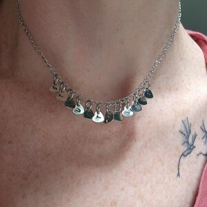 May include: A silver necklace with a chain and multiple small heart-shaped charms. Each charm has a letter engraved on it, spelling out the word "TRUST".