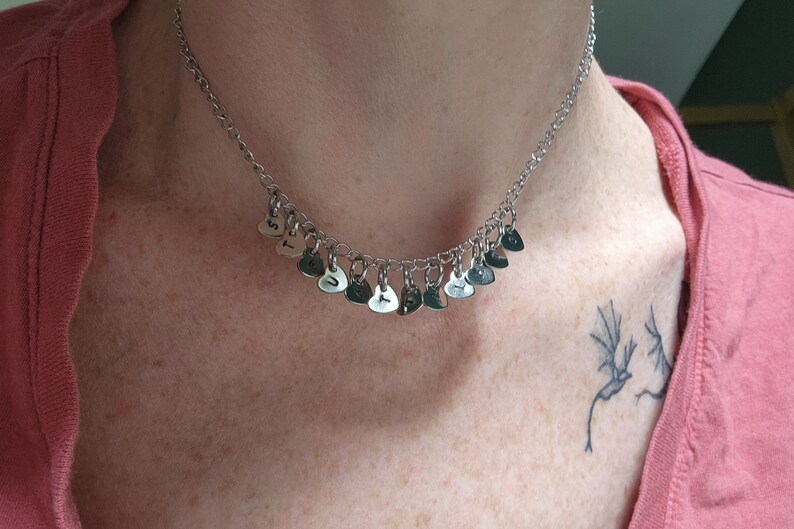May include: A silver necklace with a chain and multiple small heart-shaped charms. Each charm has a letter engraved on it, spelling out the word "TRUST".