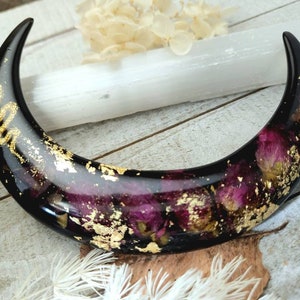 May include: Black crescent moon shaped resin dish with gold leaf and dried pink flowers embedded inside.