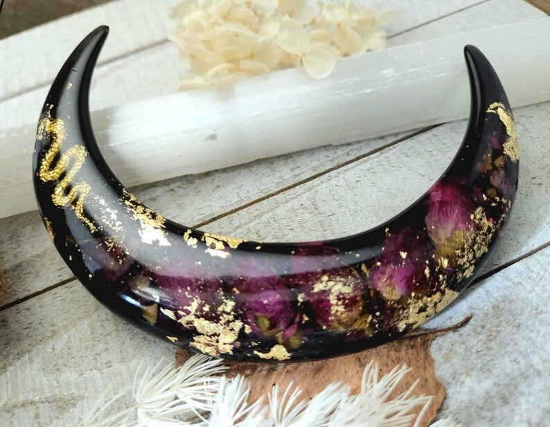 May include: Black crescent moon shaped resin dish with gold leaf and dried pink flowers embedded inside.