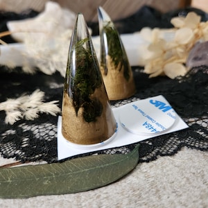 May include: Two gold and green resin horns with a clear resin base. The horns are attached to a white backing with double-sided tape.