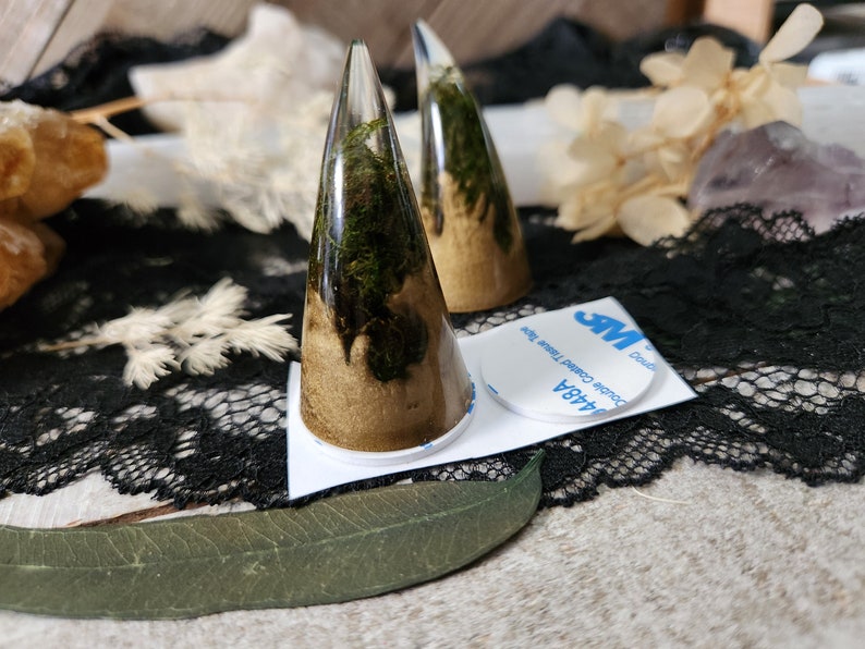 May include: Two gold and green resin horns with a clear resin base. The horns are attached to a white backing with double-sided tape.