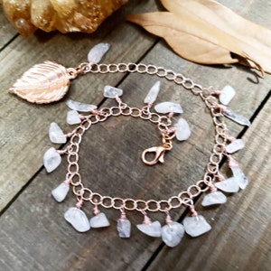May include: A rose gold chain bracelet with a leaf charm and dangling clear quartz stones.