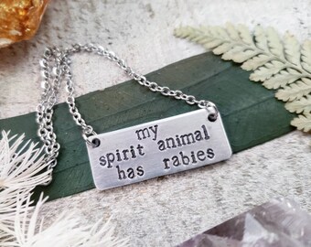 May include: A silver necklace with a rectangular pendant that reads "my spirit animal has rabies".