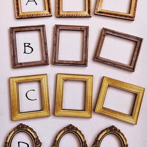 Puede incluir: Nueve marcos de fotos decorativos en varios estilos y colores están dispuestos sobre un fondo blanco. Los marcos incluyen formas cuadradas y ovaladas, con diseños ornamentados y sencillos. Las letras A, B, C y D son visibles en algunos marcos.