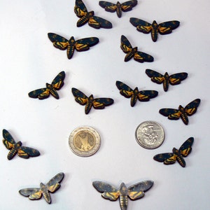 May include: A collection of 12 wooden butterfly cutouts with black and green wings and yellow accents. The butterflies are arranged in a random pattern on a white surface.