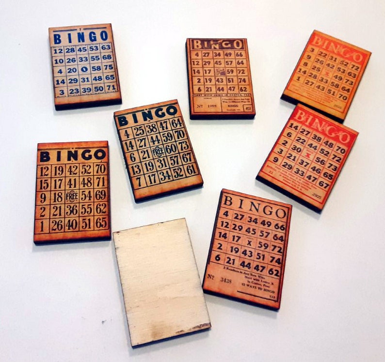 May include: Seven wooden bingo cards with black numbers and the word "BINGO" printed in a red banner. The cards are on a white surface.