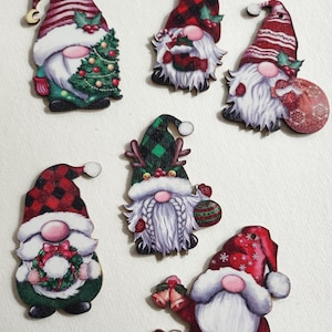 May include: Six wooden Christmas ornaments shaped like gnomes. Each gnome is wearing a different hat and holding a different Christmas-themed item. The gnomes are painted in various colors, including red, green, white, and black.